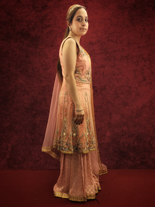 A pink indo-western ensemble featuring a net peplum top adorned with zarkan and beads, paired with a luxurious khaddi banarsi gharara, exudes a blend of contemporary flair and classic elegance.